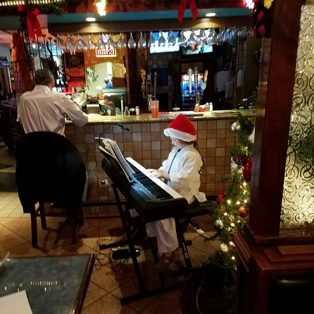 I provide entertainment playing Christmas and Holiday music every year at a family Italian restaurant and invite my students to sit in and play some Christmas songs.  Here's a young little "Santa" musician playing by the Christmas tree.